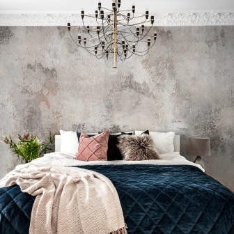 Tapet 3D Patina, cu aspect de beton, într-un dormitor cu pat dublu, cu lenjerie de pat albastră, perne decorative și o canapea cu o pătură de blană
