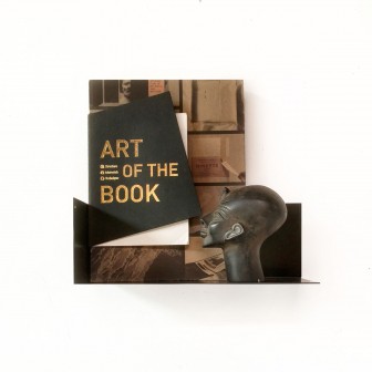 Poliță metalică neagră pentru  magnetică, montată pe perete, cu o carte și o figurină expuse pe ea.