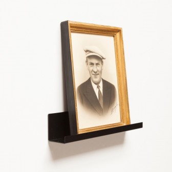 Poliță metalică neagră simplă pentru magnetic, montată pe perete cu o ramă foto pe ea.