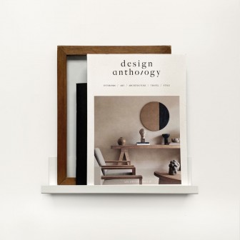 Poliță metalică simplă pentru perete, albă, cu un design minimalist. Pe ea sunt așezate un cadru, o carte și o figurină.