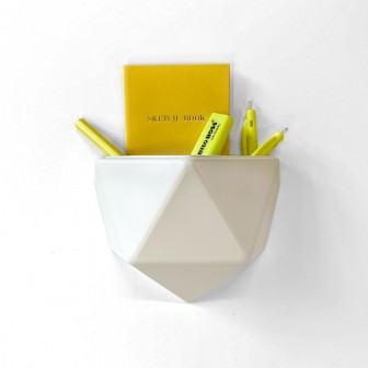 Ghiveci din plastic alb, cu design geometric, atașat pe un perete alb, conținând un carnet galben și markere galbene.