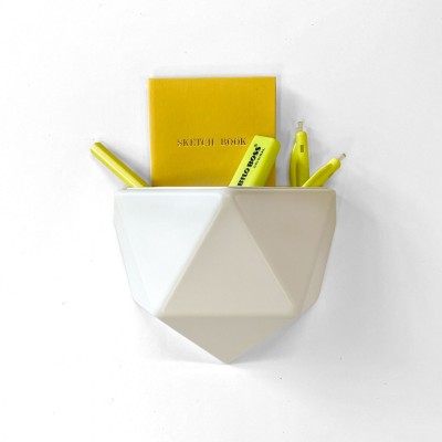 Ghiveci din plastic alb, cu design geometric, atașat pe un perete alb, conținând un carnet galben și markere galbene.
